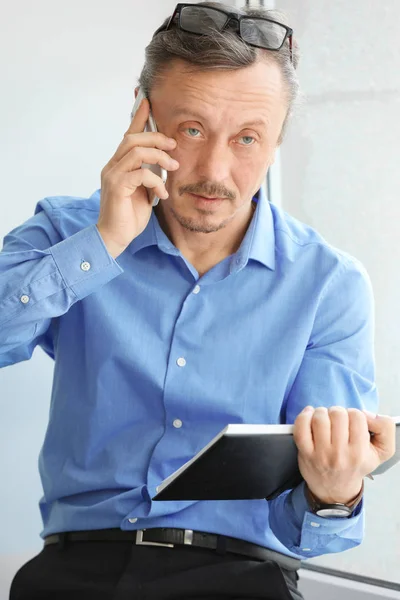 Mature man talking on mobile phone while working indoors — Stock Photo, Image