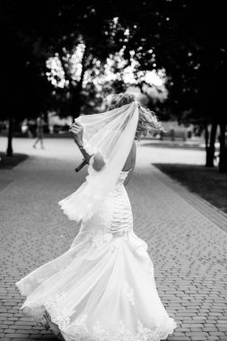 Gelin beyaz elbiseli bir arka sokakta parkta dönüyor. Elbise rüzgarda geliştirir. Bir gelinlik mutlu gelin dönüyor.