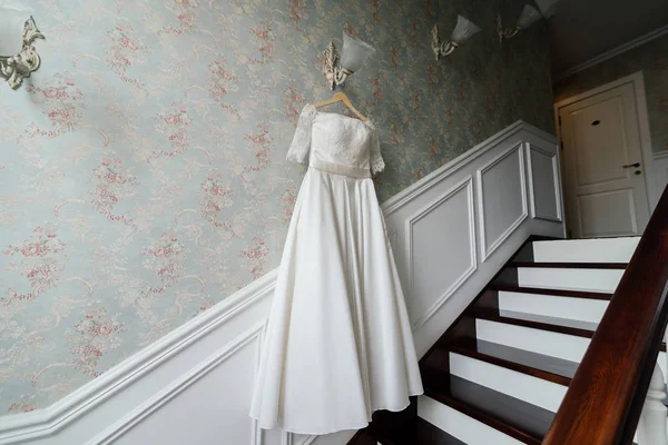 Vestido de noiva creme pendurar na lâmpada contra a parede ao lado das escadas do hotel — Fotografia de Stock