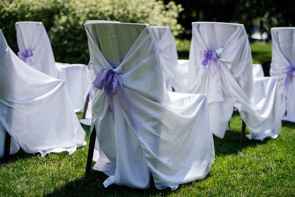 Sillas para la ceremonia con capa de satén blanco y cinta púrpura sobre una hierba verde — Foto de Stock