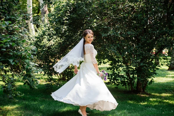 Mariée en robe blanche tourne dans le parc. La robe se développe dans le vent. Mariée heureuse dans une robe de mariée tourne — Photo
