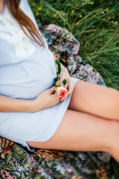 Mujer embarazada en vestido azul sentada en una manta con una rosa en la mano — Foto de Stock