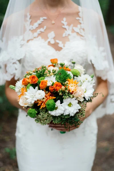 Wedding bouquet of orange roses, white and orange chrysanthemums and greenery in the bride\'s hands