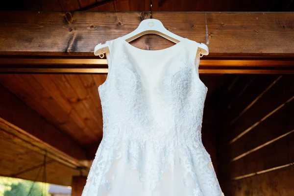 Ein wunderschönes cremefarbenes Hochzeitskleid hängt an der Wand neben dem Holzhaus — Stockfoto