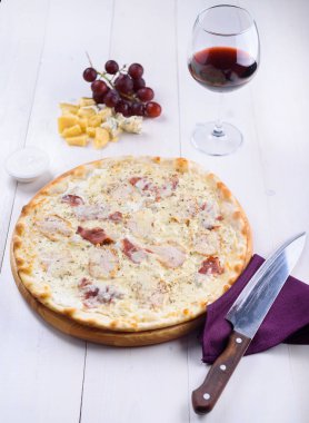 Pizza bianca tavuk, jambon ve yanında bir kadeh şarap, üzüm ve peynir parçalarını ahşap bir gemide krema sos ile