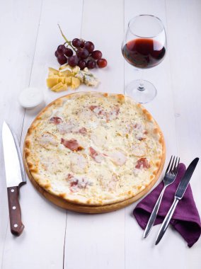 Pizza bianca tavuk, jambon ve yanında bir kadeh şarap, üzüm ve peynir parçalarını ahşap bir gemide krema sos ile