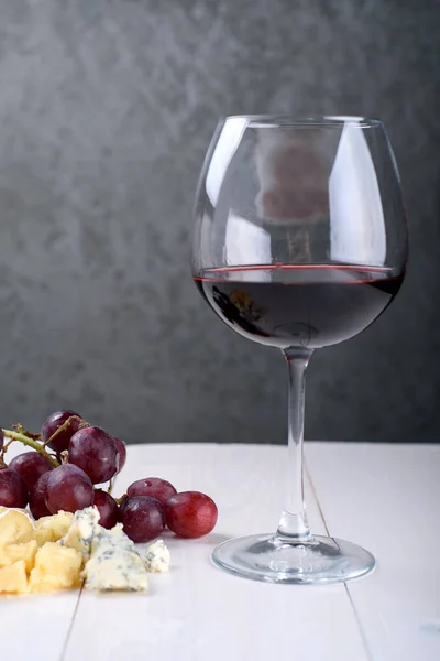 A glass of red wine, a bunch of grapes and cheese on the table — Stock Photo, Image