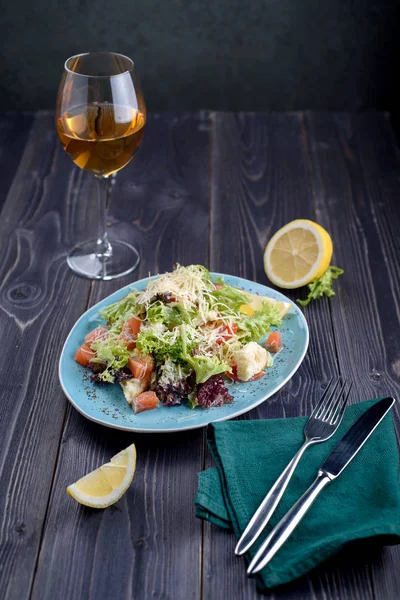 Salada Caesar com salmão em uma placa azul em uma mesa de madeira e um copo de vinho — Fotografia de Stock