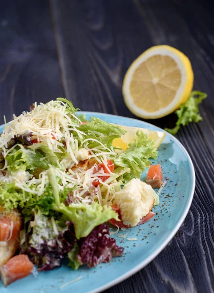 Salada Caesar com salmão em uma placa azul em uma mesa de madeira perto do limão — Fotografia de Stock