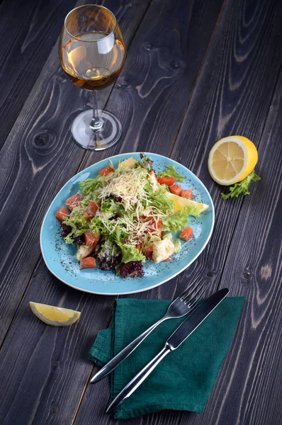 Salada Caesar com salmão em uma placa azul em uma mesa de madeira e um copo de vinho — Fotografia de Stock