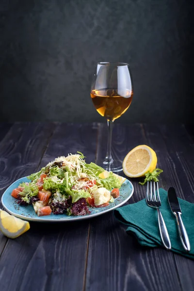 Salada Caesar com salmão em uma placa azul em uma mesa de madeira e um copo de vinho — Fotografia de Stock