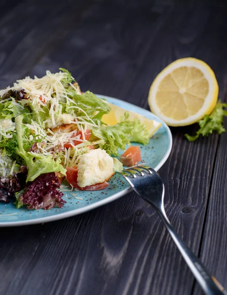 Salada de Caesar com salmão em uma chapa azul em uma mesa de madeira . — Fotografia de Stock