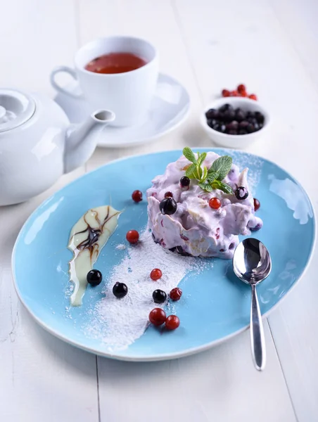 Cake with fresh berries on a blue plate next to a cup of tea and a teapot. Berry cake with tea