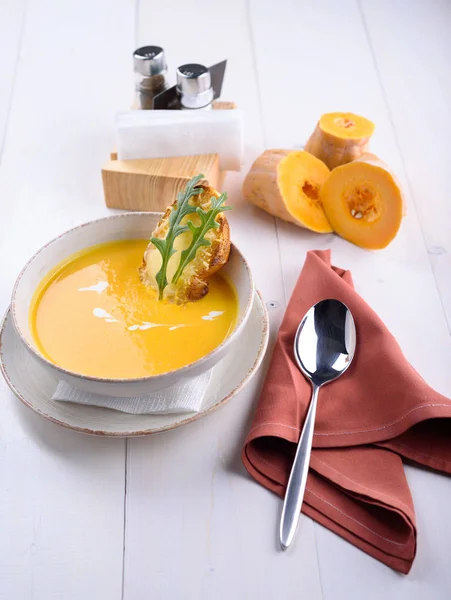 Zuppa di crema di zucca con pane tostato al parmigiano in un piatto bianco. Pezzi di zucca su un tavolo bianco. Pranzo al ristorante — Foto Stock