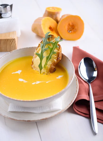 Zuppa di crema di zucca con pane tostato al parmigiano in un piatto bianco. Pezzi di zucca su un tavolo bianco. Pranzo al ristorante . — Foto Stock