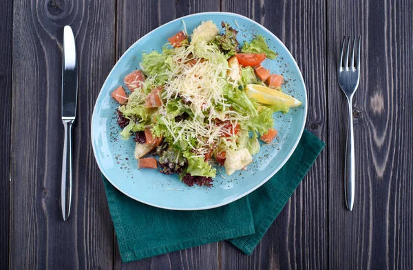 Sezar salatası somon ahşap bir masa üzerinde mavi bir plaka ile. — Stok fotoğraf