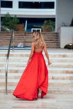 Merdivenlerden yukarı yürümek uzun Kırmızı elbiseli uzun kıvırcık saçlı bir kız. Kırmızı elbiseli kız. Uzun kırmızı elbise rüzgârda çırpınıyor