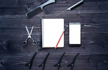 Kuaför araçlar ahşap arka plan üzerinde. Kuaför araçlarıyla düz boş kartı yatıyordu. Üstten görünüm makas, tarak ve toka ile boş defter, kalem ve telefon, boş alan ahşap tablo