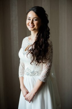 Güzel genç gülümseyen gelin damat için kapalı bekliyor beyaz elbiseli. Zarif çekici genç esmer gelin kapalı bir gelinlikli poz. Sabah, Gelin