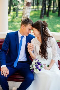 Güzel genç gelin ve damat bir bankta oturan ve elele. Evlilik çift, düğün günü aşık