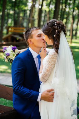 Gelin ve damat öpüşme. Güzel genç gelin ve damat öpüşme ahşap Bank Park yakınındaki. Evlilik çift, düğün günü aşık