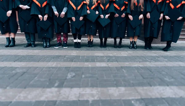 Graduates holding their hats in hands. Graduates wearing robes and hats in their hands. Group of  students in bachelor gowns