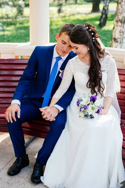 美丽的年轻新娘和新郎坐在长椅上牵着手 婚礼情侣恋爱在婚礼当天 — 图库照片