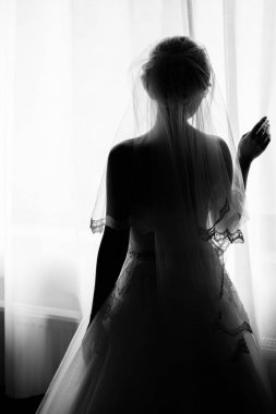Güzel gelin silüeti pencerenin önünde duran ve perdeleri tutarak. Sabah gelin. Güneş ışığı altında vasıl pencere sabah poz peçe içinde gelin. Hazırlanıyorum. Siyah ve beyaz fotoğraf