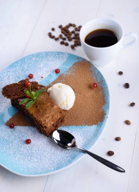 Bir fincan kahve yanındaki mavi tabakta dondurma ile çikolatalı kek