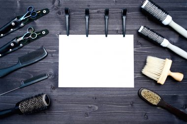Kuaför araçlar ahşap arka plan üzerinde. Kuaför araçlarıyla düz boş kartı yatıyordu. Makas, tarak, fırçaları ve boş beyaz kağıt, boş alan ile toka ile ahşap masa üzerinde üstten görünüm