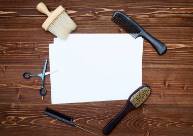 Kuaför araçlar ahşap arka plan üzerinde. Kuaför araçlarıyla düz boş kartı yatıyordu. Makas, tarak ve fırça ile boş beyaz kağıt, boş alan ahşap masa üzerinde üstten görünüm