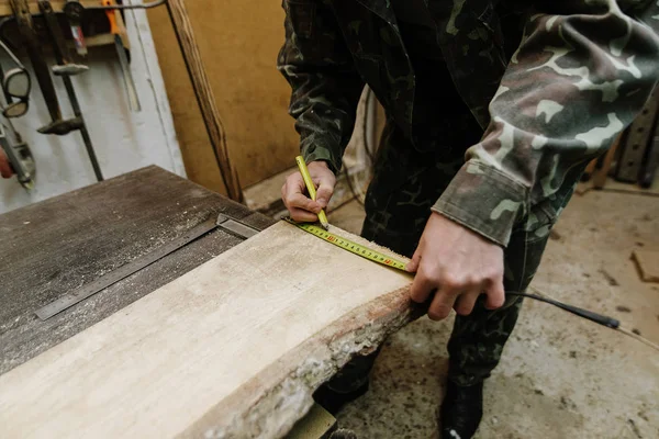 Pencil in the carpenter\'s hand. Carpenter measures the width of the board with a tape measure in the workplace