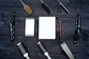 Kuaför araçlar ahşap arka plan üzerinde. Kuaför araçlarıyla düz boş kartı yatıyordu. Üstten görünüm makas, tarak ve toka ile boş defter, kalem ve telefon, boş alan ahşap tablo
