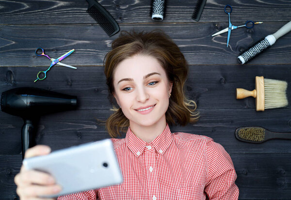 Happy smiling young woman in plaid shirt with hairdresser tools among her taking selfie