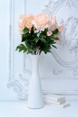 Beyaz kitaplar yanında beyaz bir vazo içinde yapay pembe peonies. Beyaz bir Vazoda Çiçekler bileşimi