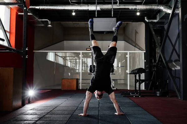 Athlete walking on his hands standing upside down in gym. Man doing push ups on his hands. Crossfit training. Workout lifestyle concept.  Full body length portrait