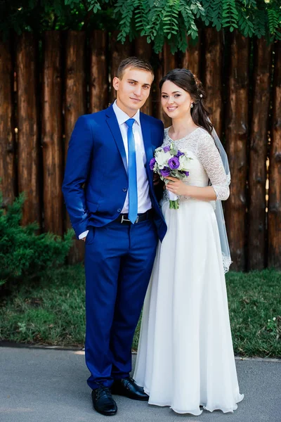 The bride and groom near the wooden wall from logs in the park. Wedding couple in love at wedding day — Stock Photo, Image