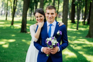 Yong gülümseyen güzel gelin ve damat hugs parkta. Gelin Damat kucaklar. Evlilik çift, düğün günü aşık