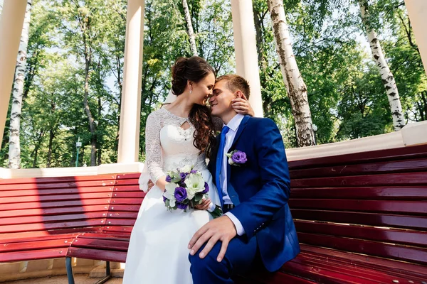 A noiva e o noivo sentam-se em um banco — Fotografia de Stock