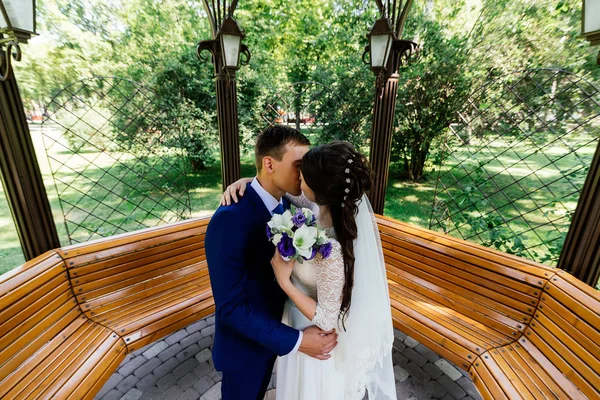 The bride and groom kiss in the arbour. Wedding couple in love at wedding day in the park — Stock Photo, Image