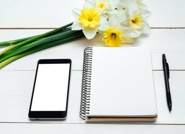 Nergis Beyaz ahşap zemin üzerine sarı buket. Boş kart düz yatıyordu. Nergis, boş günlüğü, kalem ve telefon, boş alan tablo üstten görünüm