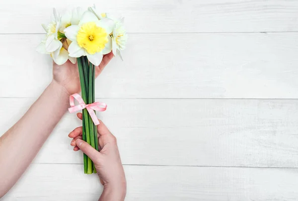 Yellow bouquet of narcissus in woman hands on white background. Flat lay, top view, copy space. Floral background