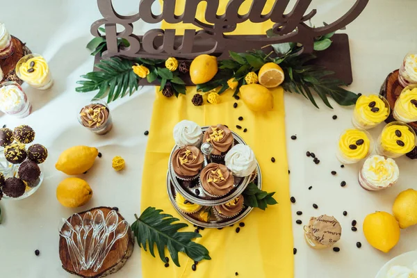 Holiday candy bar in yellow and brown color. Wedding candy bar served with cupcakes, cake pops, desserts in glasses, lemons and coffee beans