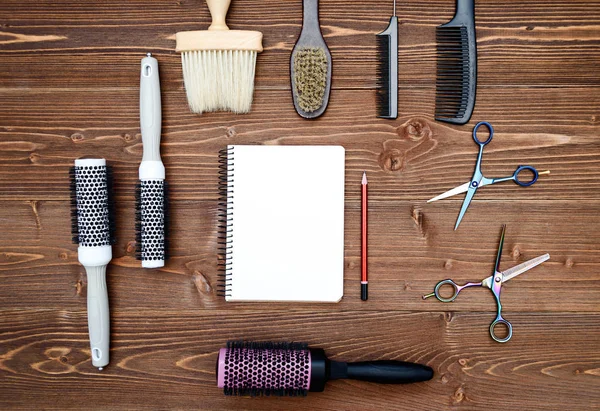 Hairdresser tools on wooden background. Blank card with barber tools flat lay. Top view on wooden table with scissors, hairbrushes and comb with empty notebook and pencil, free space