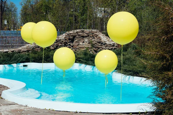 Pool with big yellow balloons outdoor. Poolside party. The balloons on water. Decorations for wedding ceremony by the pool with blue water