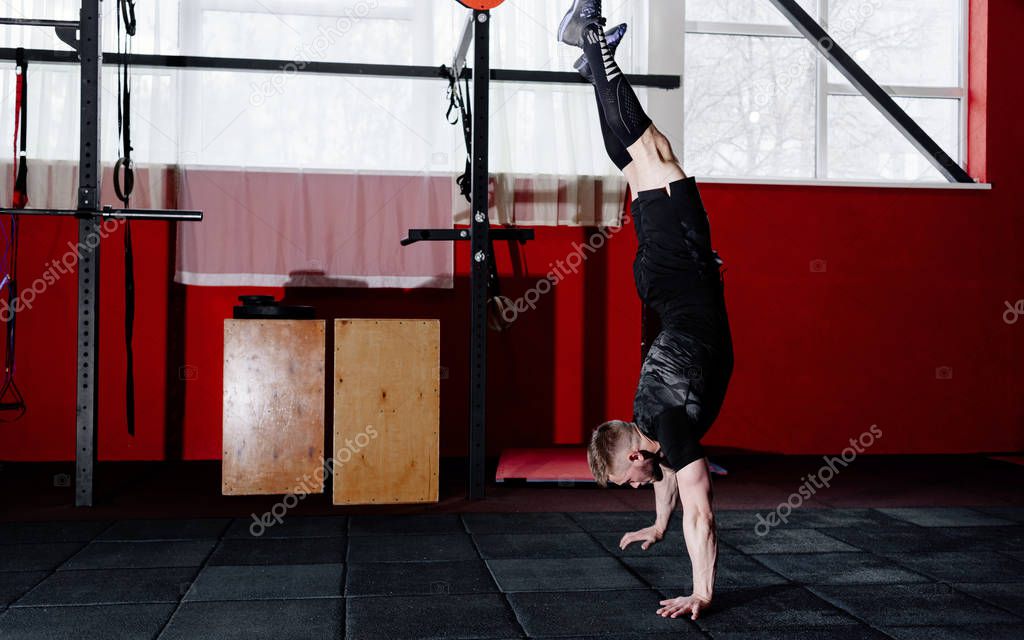 Athlete walking on his hands standing upside down in gym. Crossfit training. Workout lifestyle concept.  Full body length portrait