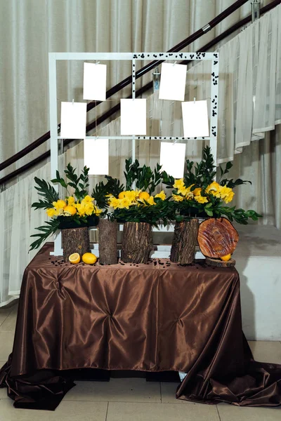 Stylish table list seating plan for wedding reception. Table wedding guests list on elegant framed board decorated with yellow daffodils, lemons and stumps with brown cloth