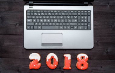 Üstten Görünüm office masa masa açık dizüstü bilgisayar ve yeni yıl 2018 işareti simgesi gingerbread çerezleri üzerinden. İş tatil kavramı. Ahşap arka plan üzerinde laptop ve Noel süslemeleri ile çalışma alanı
