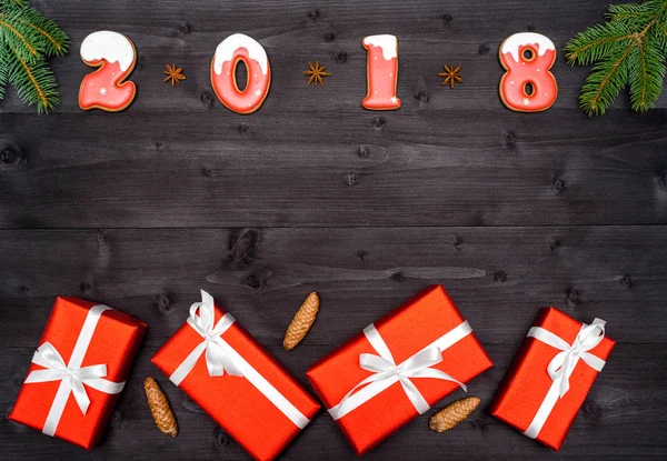 Šťastný nový rok 2018 znaménko z červených a bílých perníčky na tmavé dřevěné pozadí s červenými dárkové boxy, kopie prostor. Pohled shora, ploché ležel. Vánoční nebo novoroční pohlednice — Stock fotografie