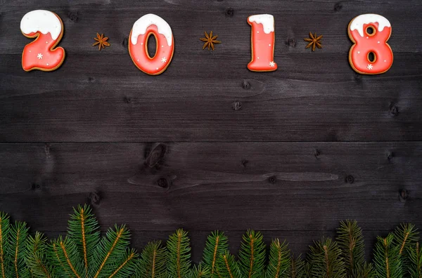 С Новым 2018 годом знак символа из красного и белого пряников печенье на темном деревянном фоне с елкой ветвей, копировать пространство. Вид сверху, плоский. Новогодняя или рождественская открытка — стоковое фото